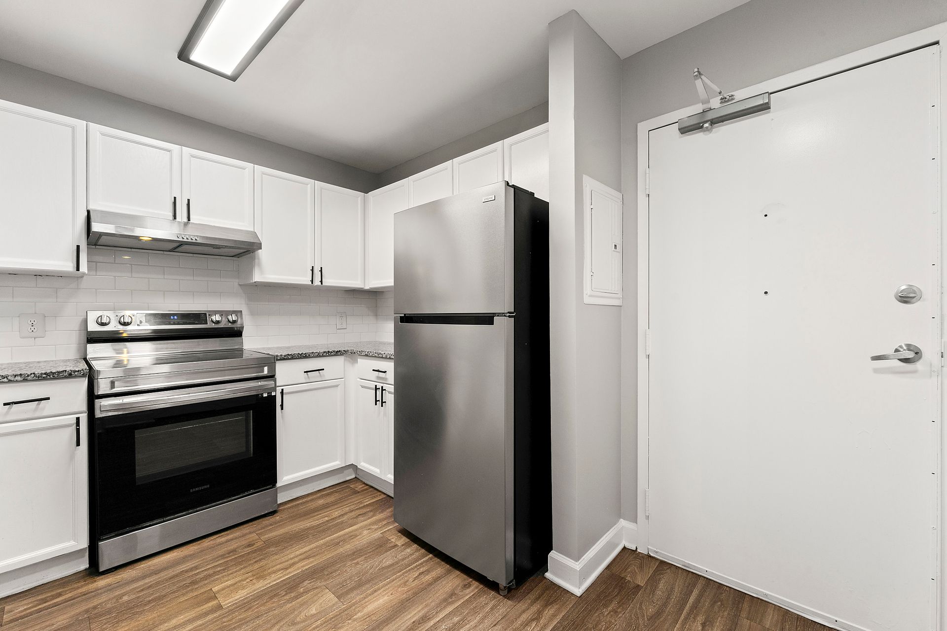 Modern kitchen with stainless steel appliances, white cabinets, and a white entry door