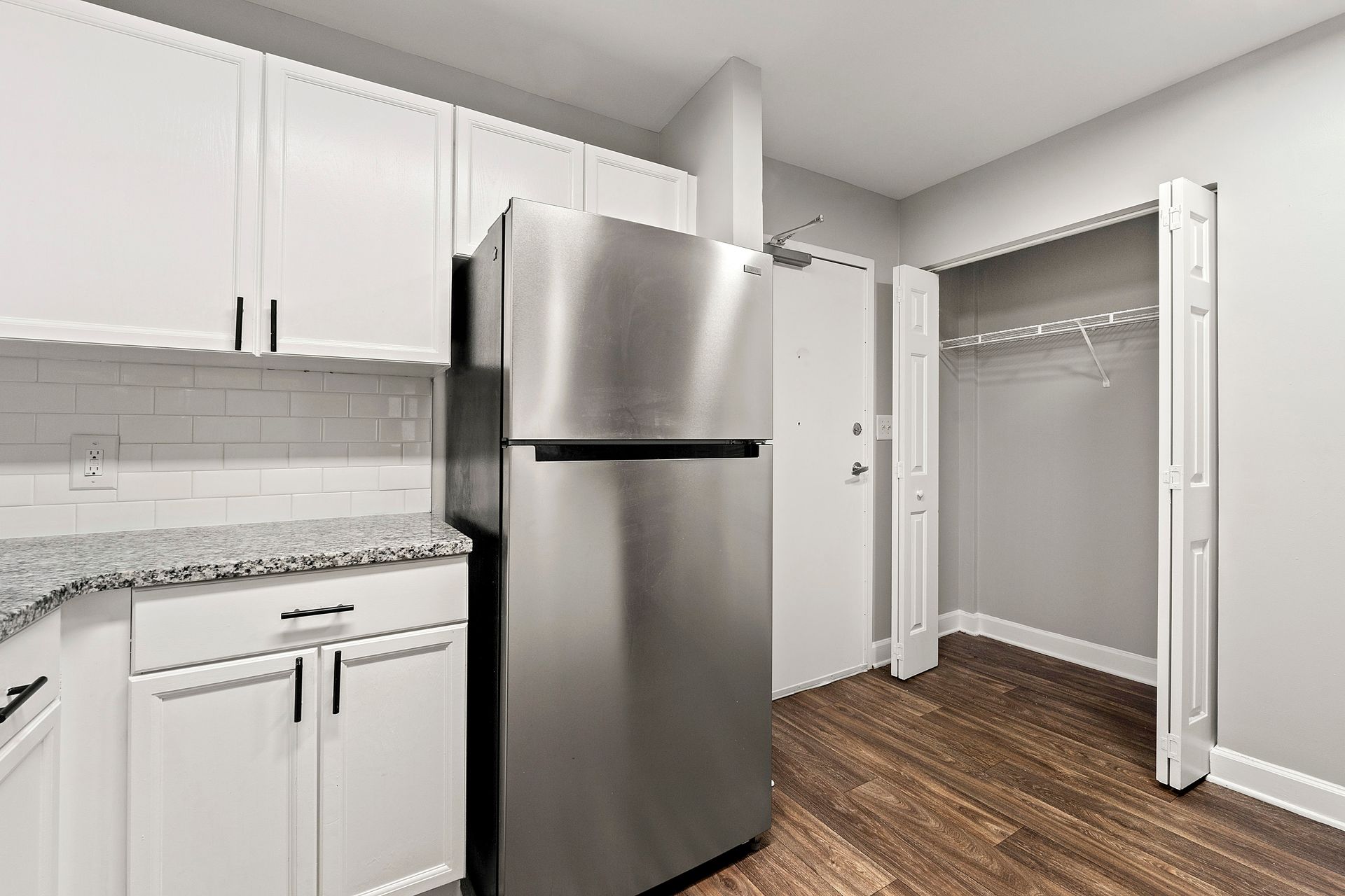 Bright kitchen with white cabinets, stainless steel fridge, gray backsplash, and open pantry closet.
