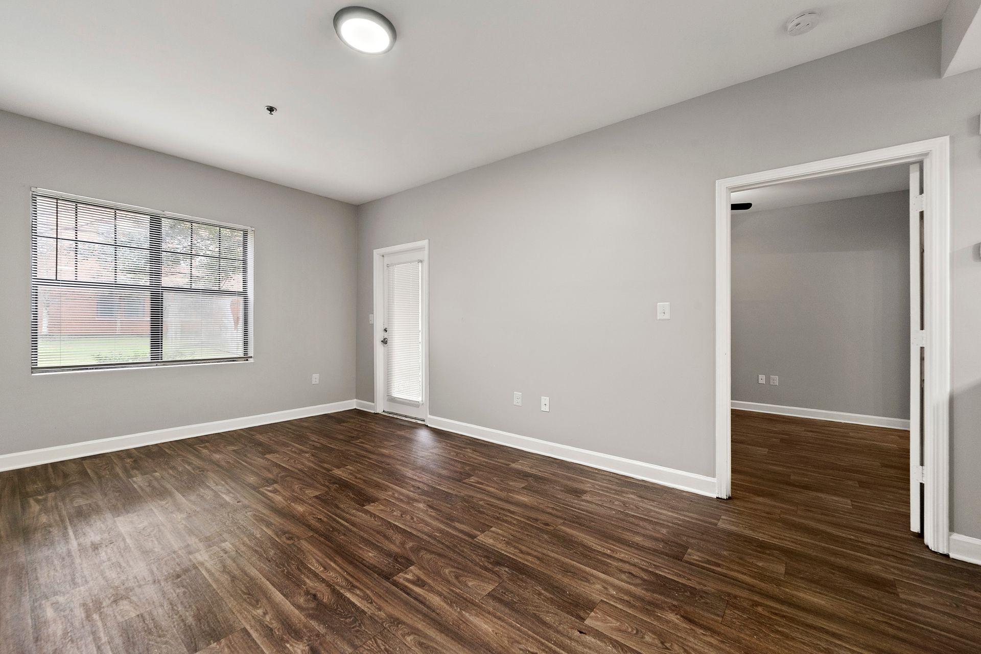 Empty gray room with dark wood floors, window, ceiling light, and open doorway