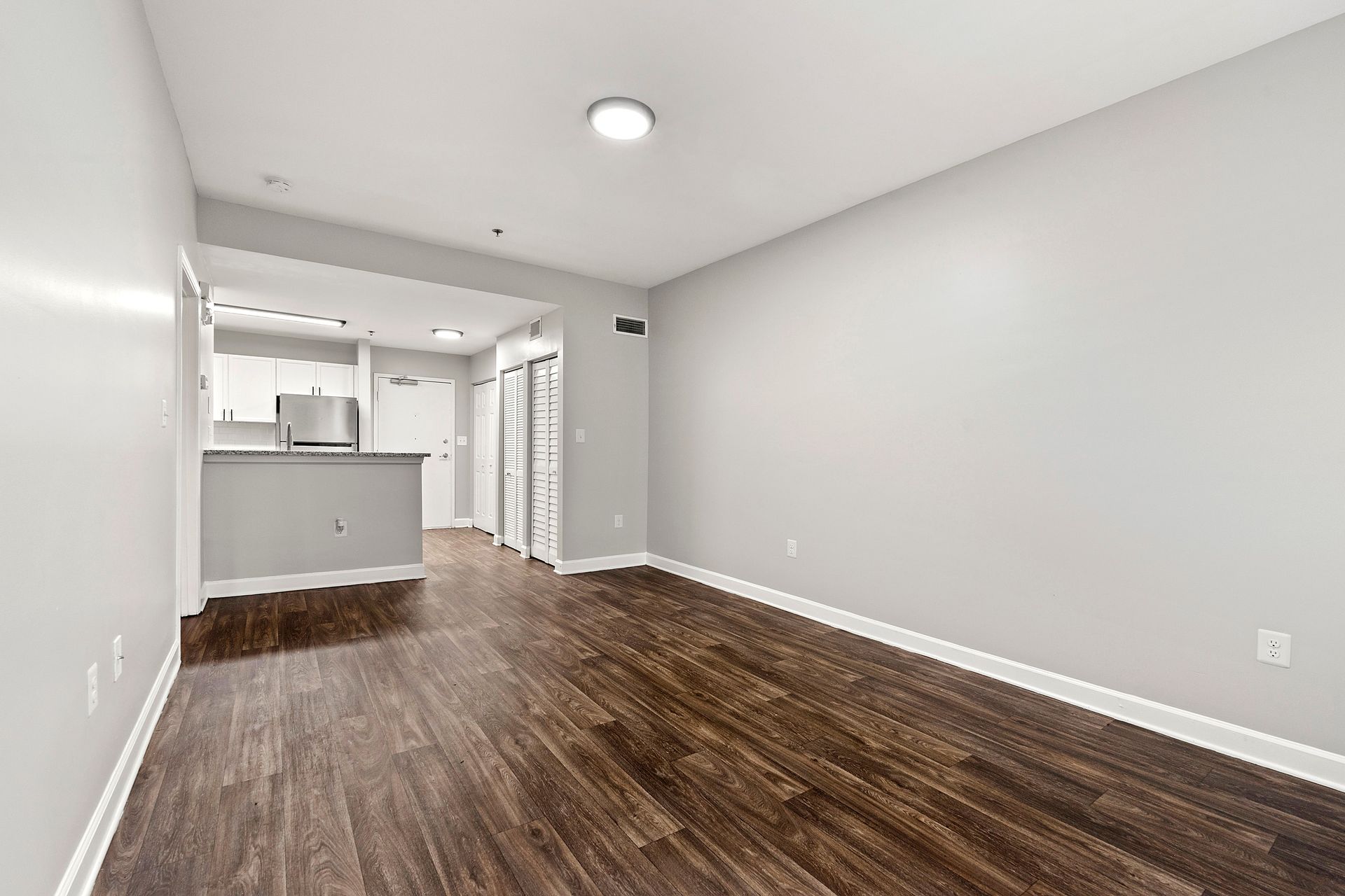 Empty modern living room with dark wood floors, white walls, and open kitchen area