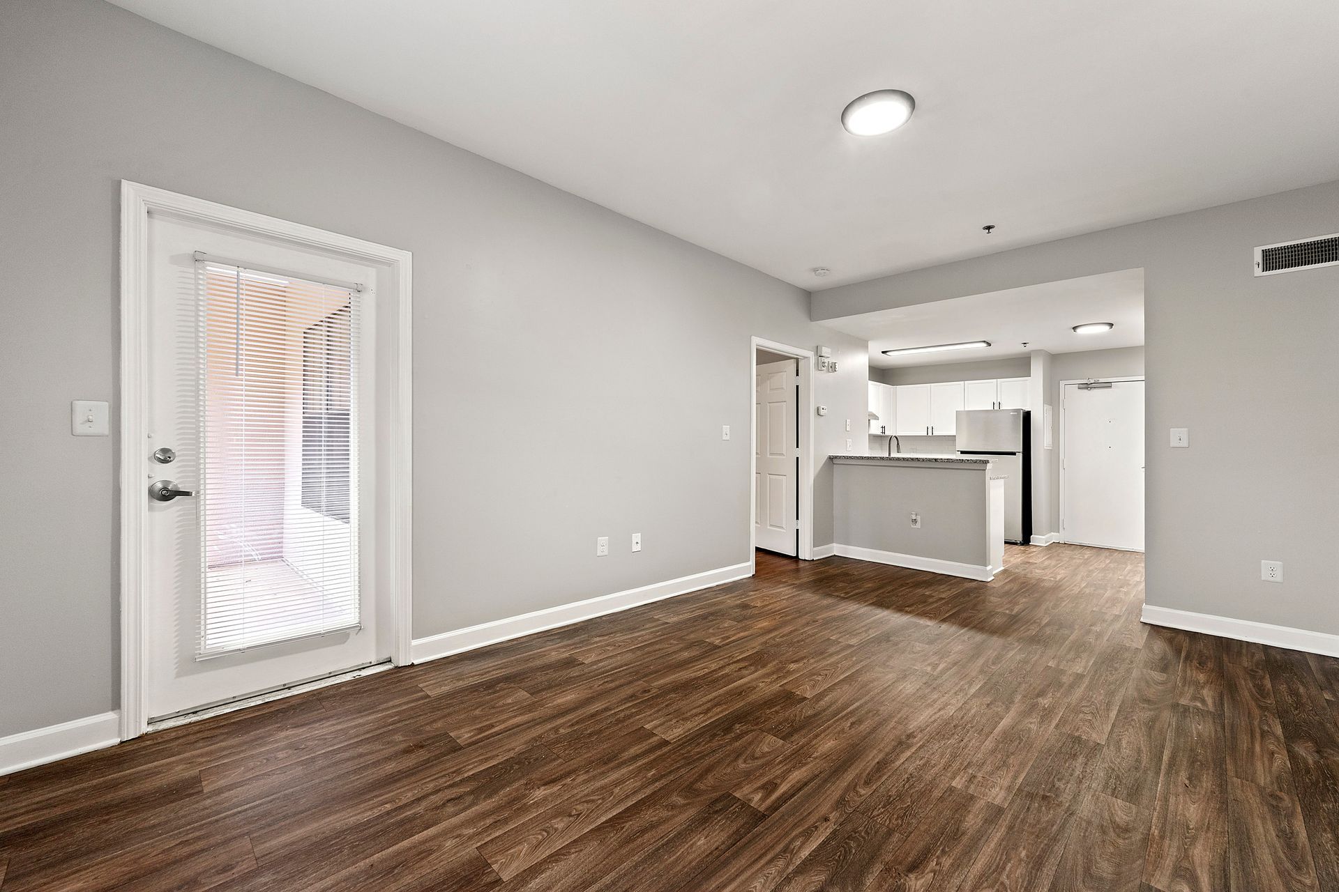 Empty open-plan living room with gray walls, wood floors, and a view into a white kitchen
