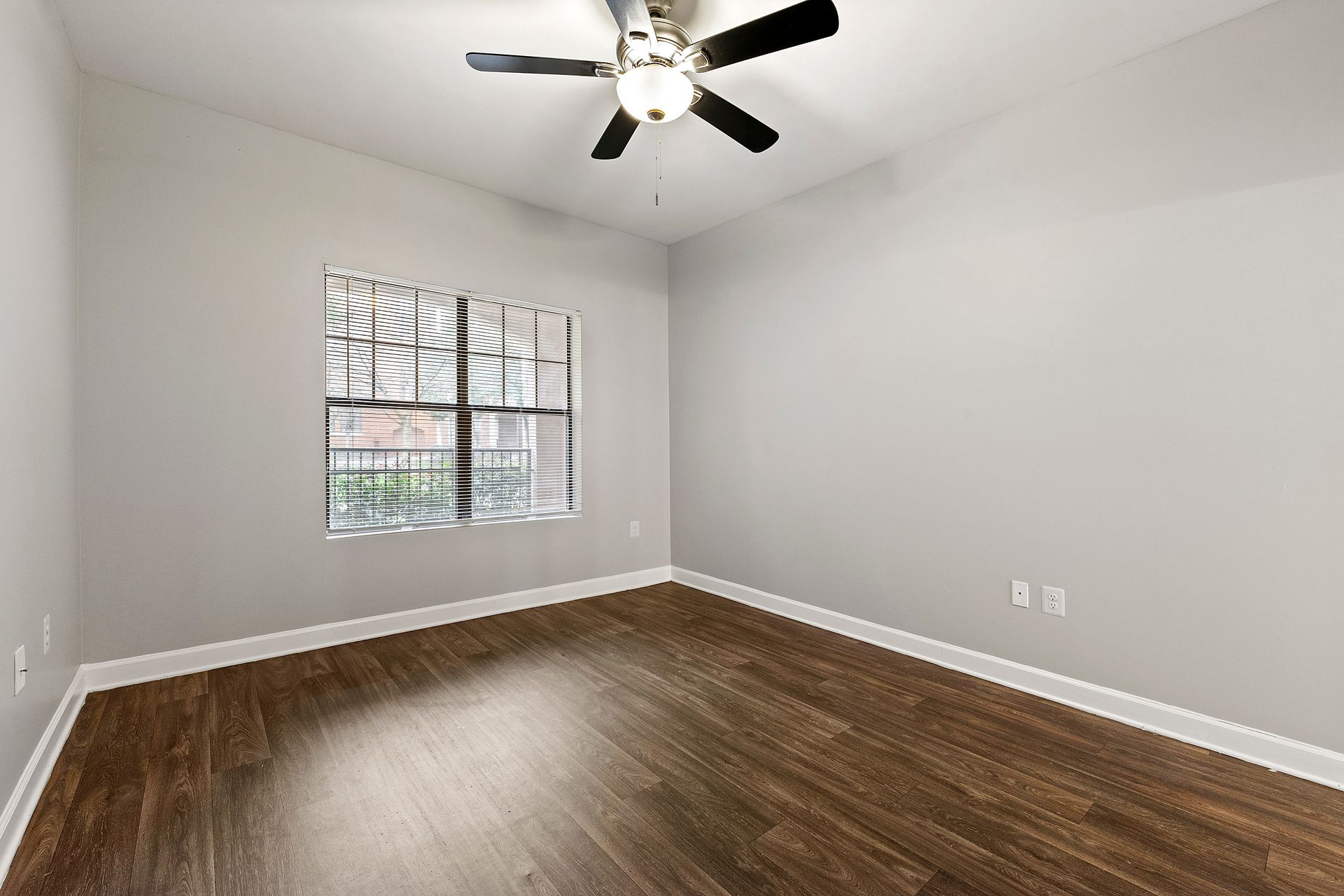Empty white bedroom with wood floor, ceiling fan, and a window with blinds