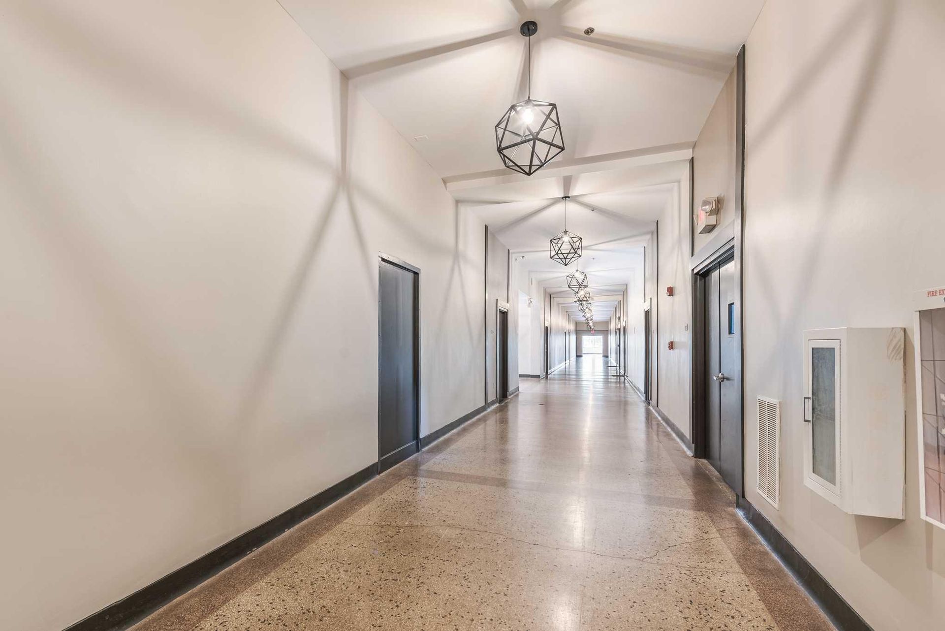 Bright white hallway with terrazzo floor, hanging lights, and doors along both sides