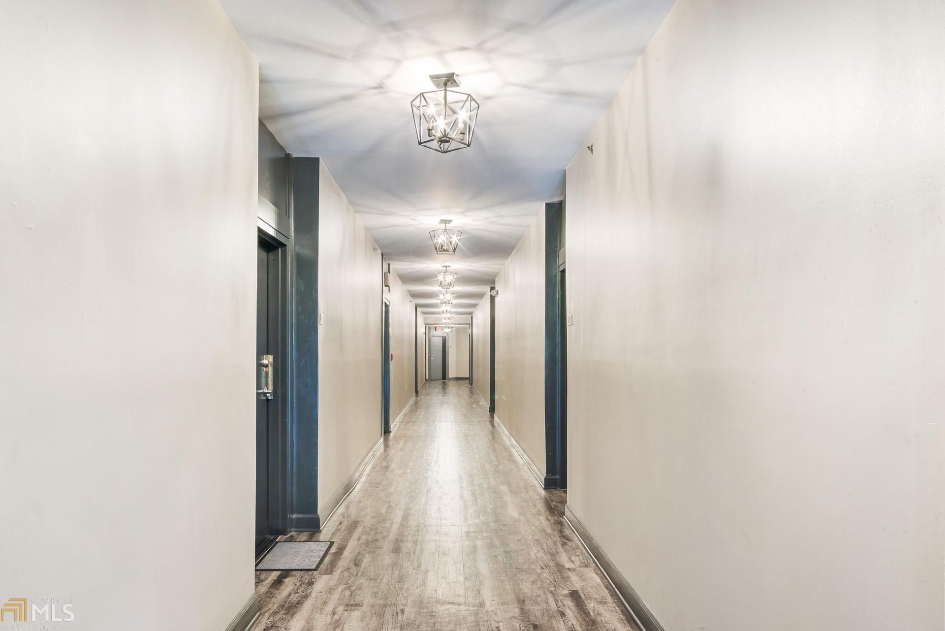 Bright, long hallway with white walls, pendant lights, and blue doors on both sides.