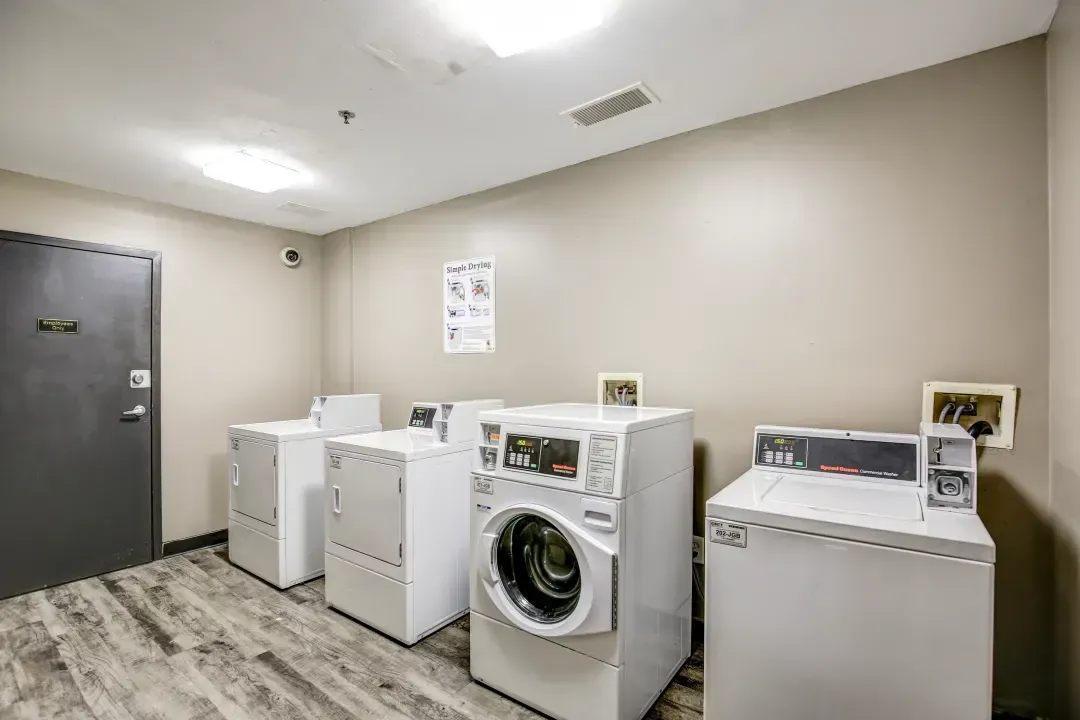Laundry room with several white washers and dryers against beige walls and gray flooring