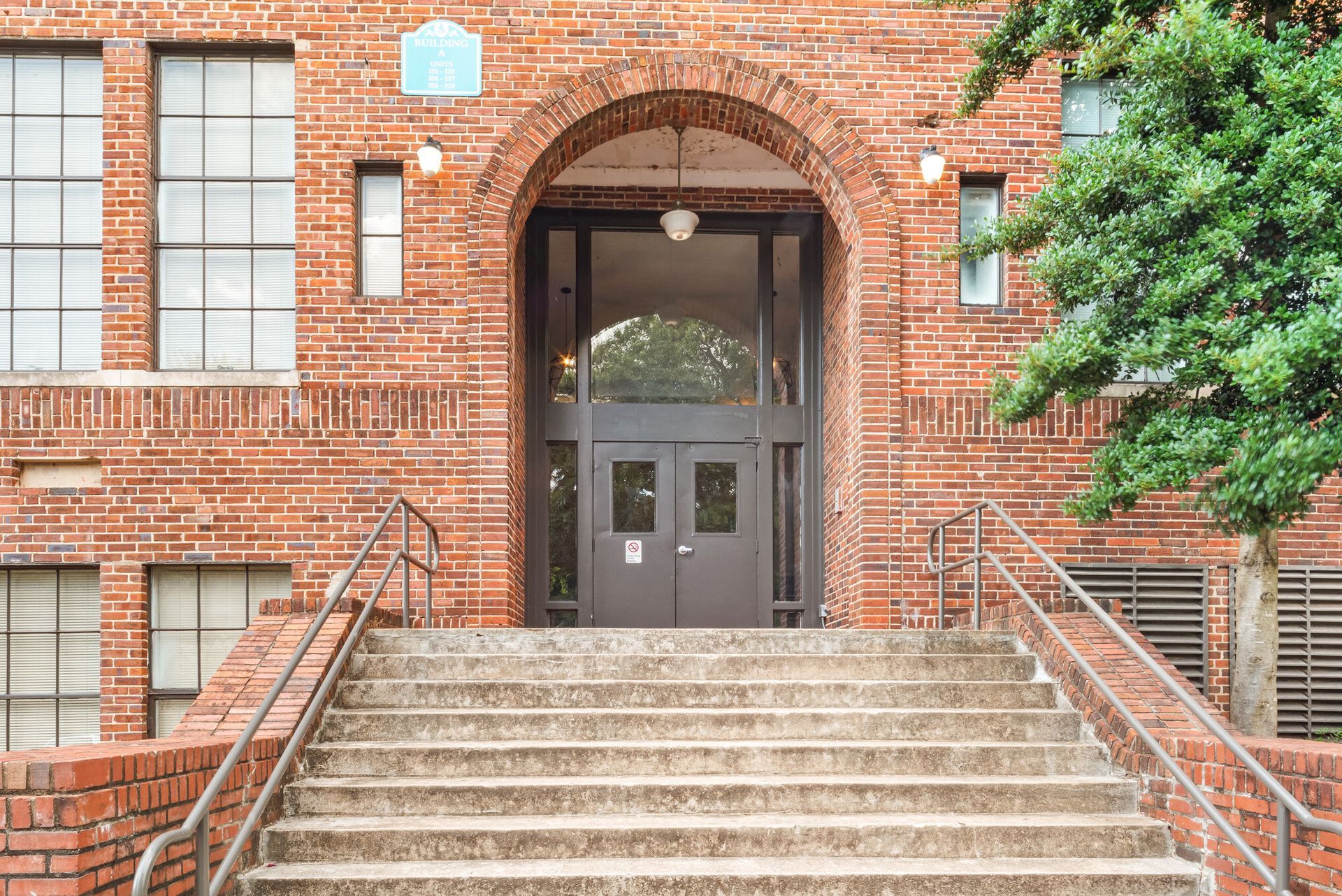 Brick building entrance with stone steps, metal railings, and dark double doors under an archway