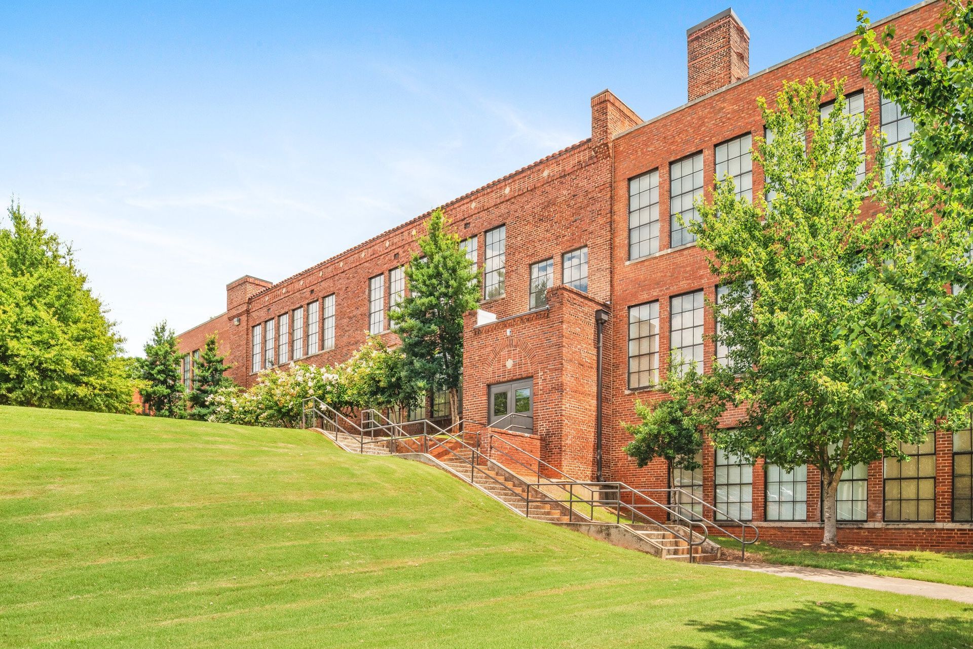 Brick apartment building beside a green lawn with trees under a bright blue sky