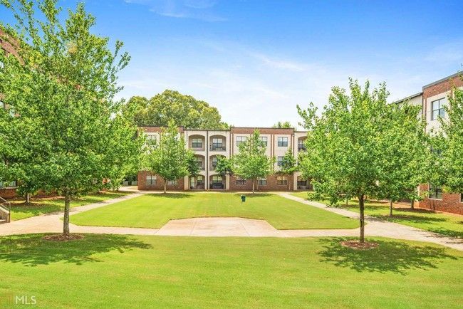 Apartment complex courtyard with green lawn, trees, and a central walkway under a clear blue sky
