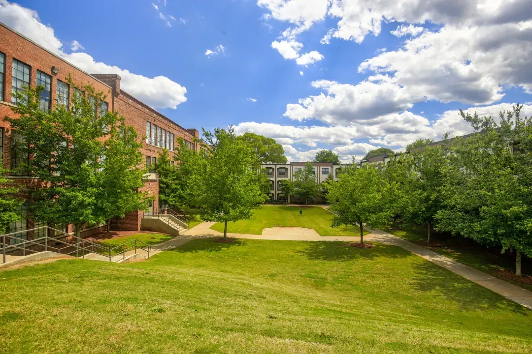 Courtyard lawn between brick buildings under a blue sky with clouds