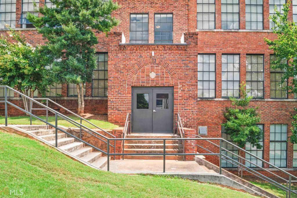 Brick apartment building entrance with stairs, railings, and a grassy slope in front
