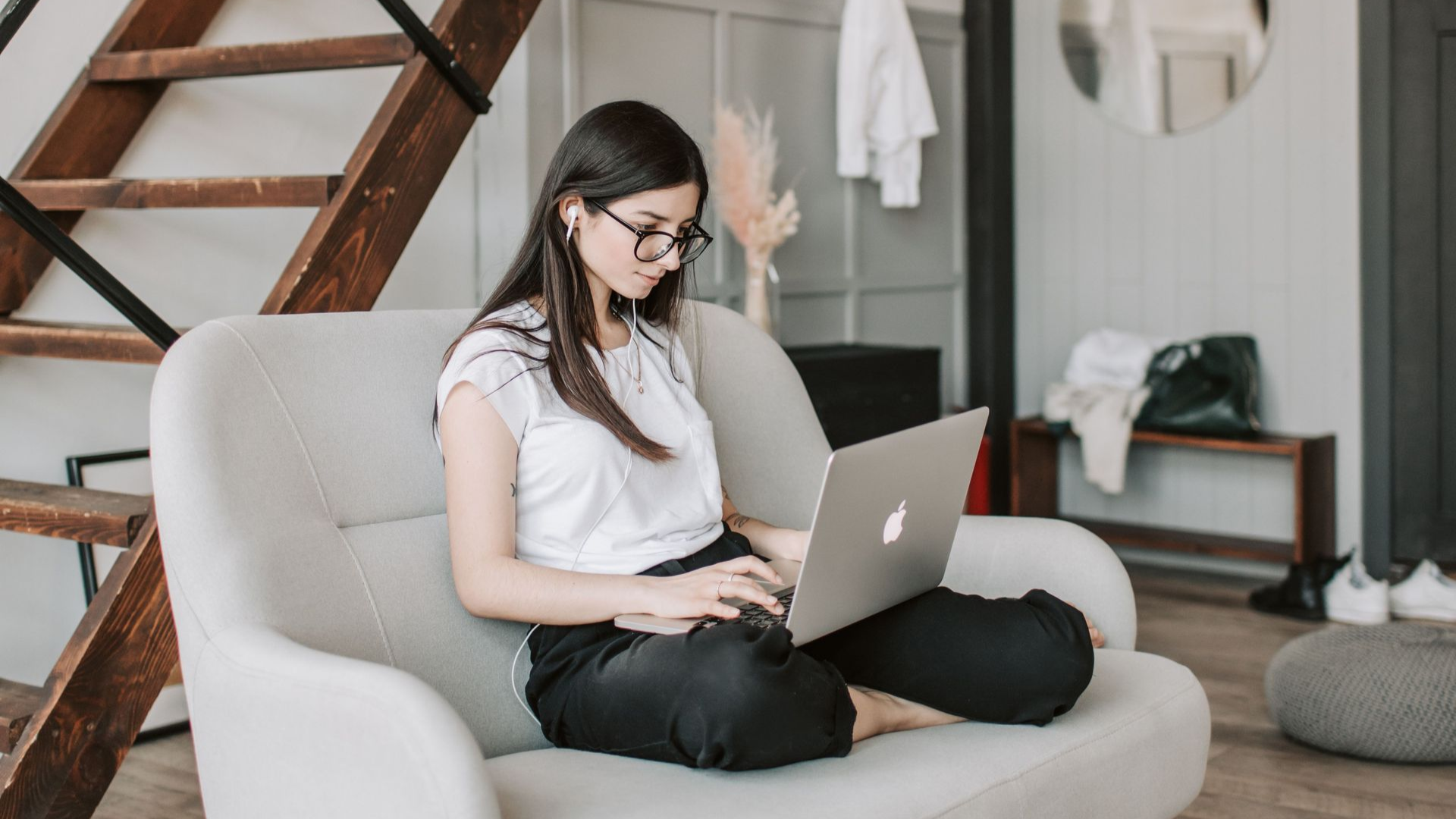 Person using a laptop on a light gray sofa in a bright living room.