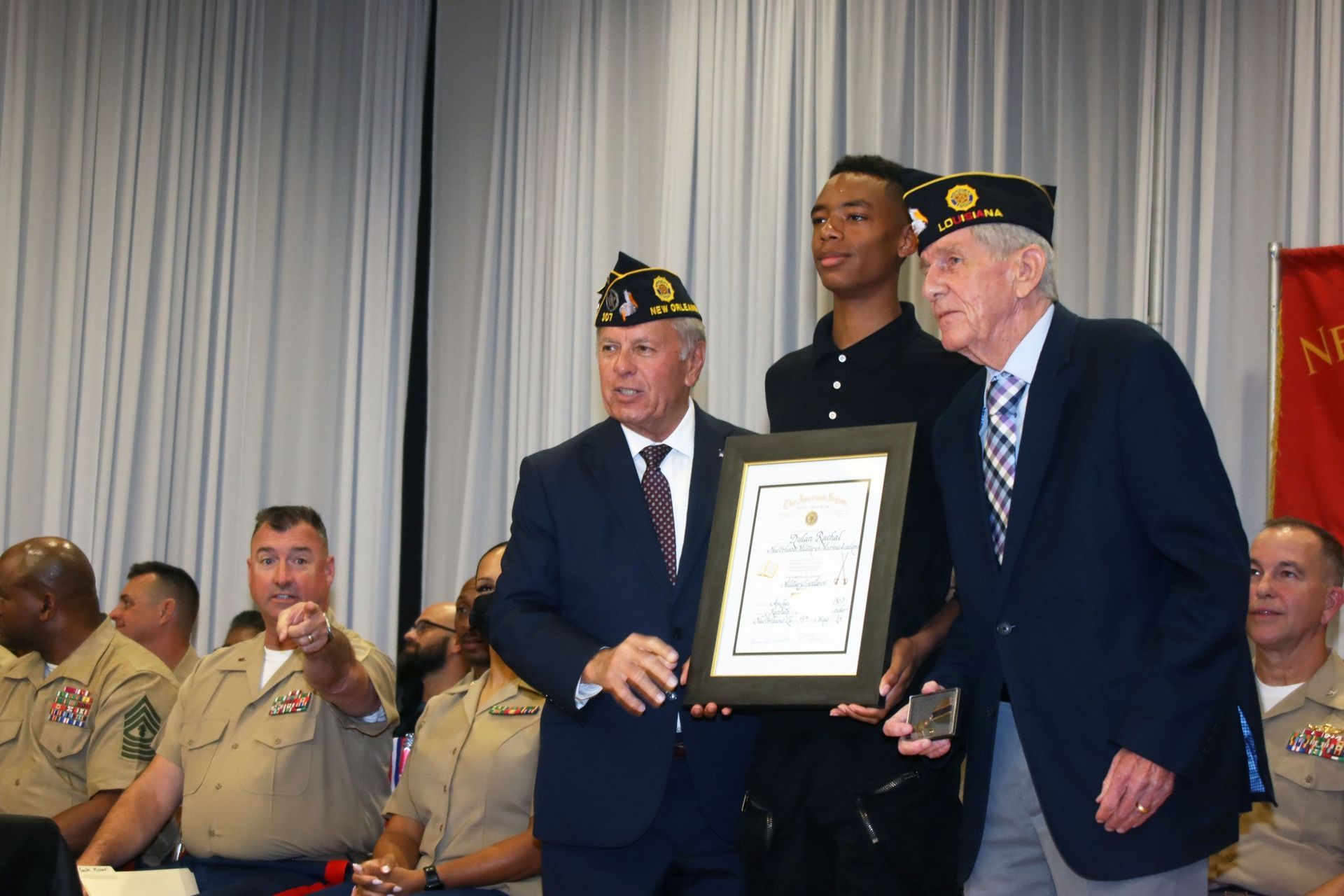 Two men in suits hold a framed certificate at a military ceremony