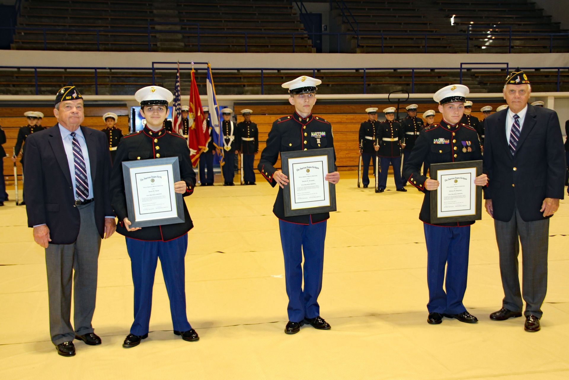 Four uniformed officers hold framed awards on a gym floor during a formal ceremony