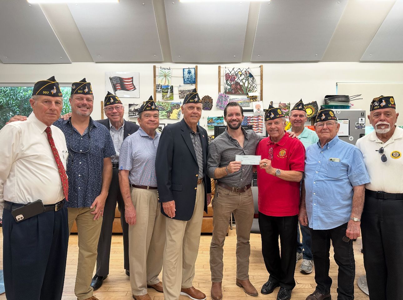 Group of veterans posing indoors, one holding a framed certificate, in front of wall posters and flags.