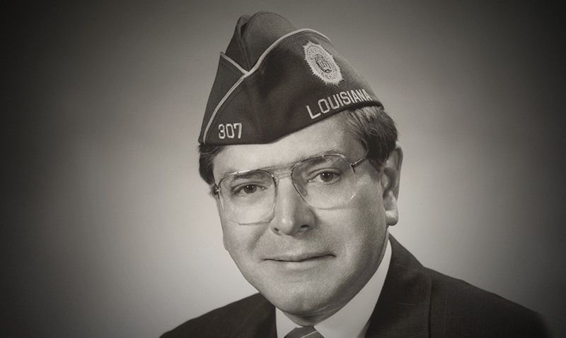 Black-and-white portrait of a man wearing a military-style cap and glasses, looking at the camera.
