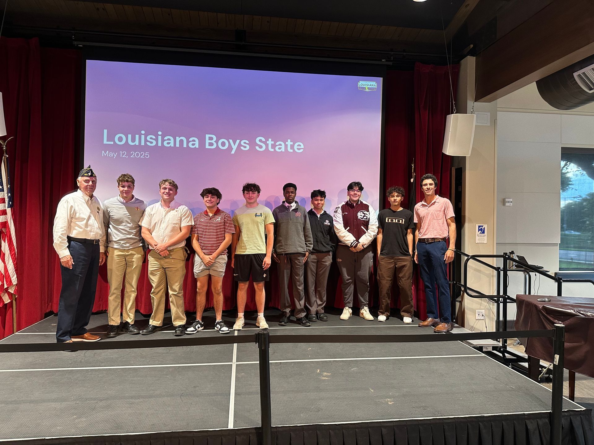 Group standing on stage at Louisiana Boys State, with a presentation screen behind them.