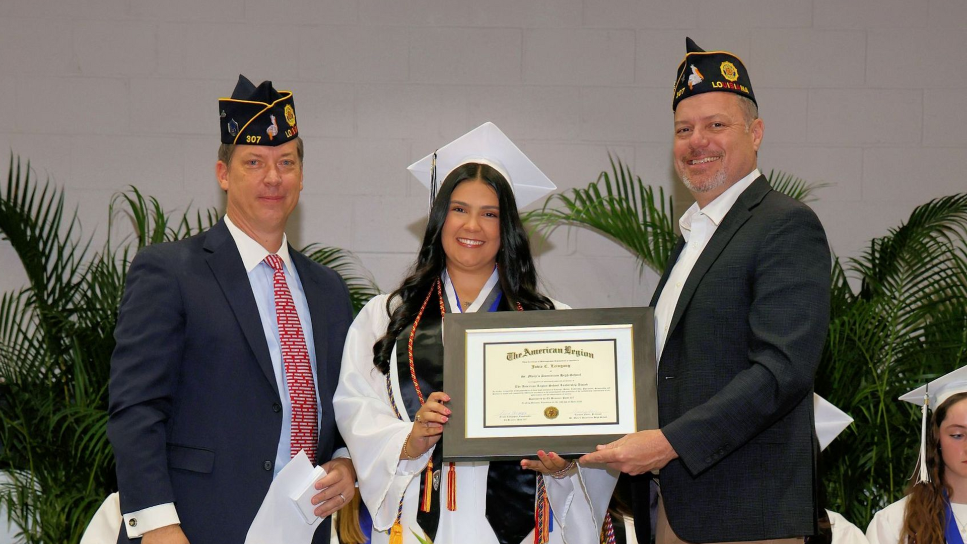 Three people in graduation caps hold a framed certificate during a ceremony