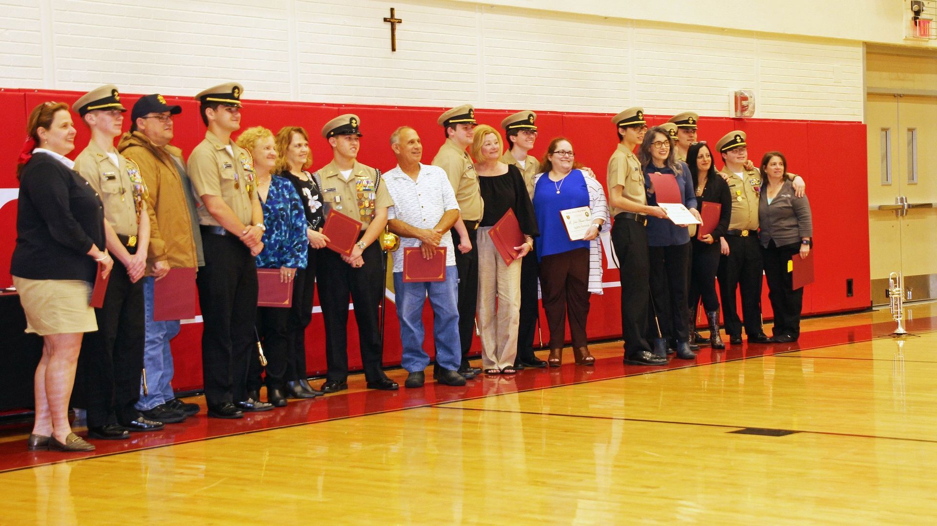People standing in a line in a gymnasium, facing forward with a red wall behind them.