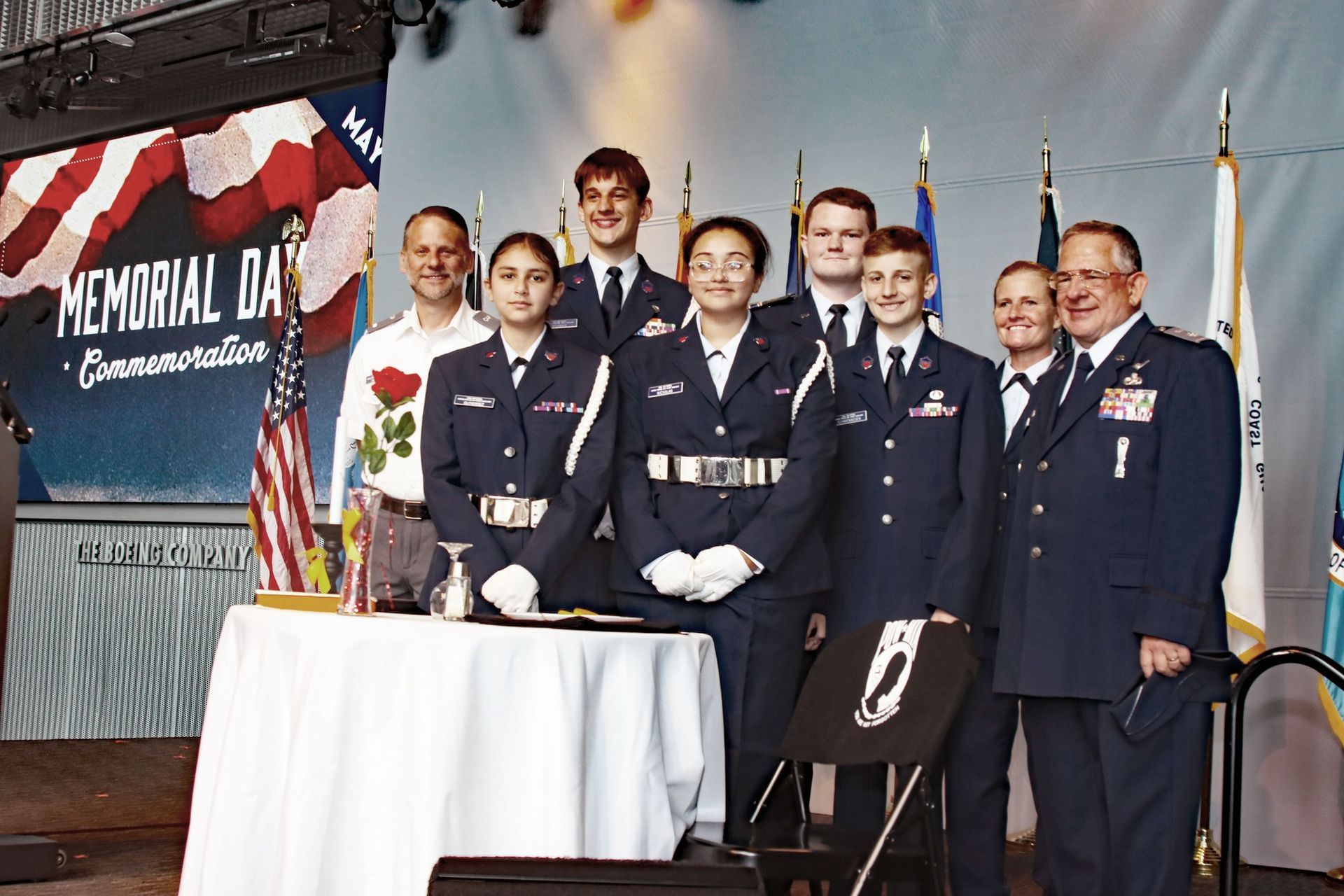 Group posing on stage in navy uniforms at a Memorial Day commemoration event