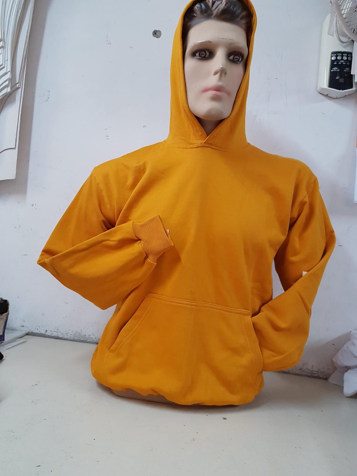 Una sudadera amarilla brillante con capucha expuesta en un maniquí sobre una pared blanca lisa.