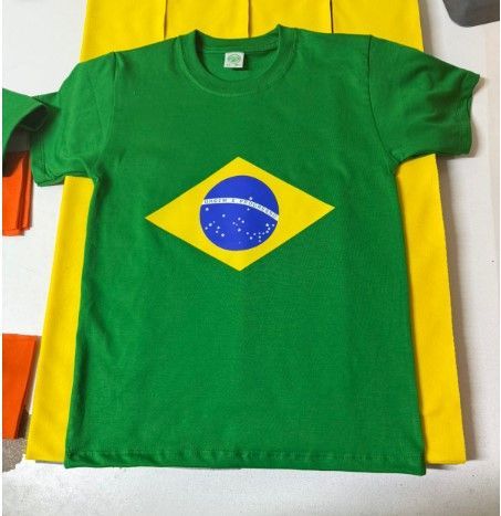 Una camiseta verde con la bandera nacional de Brasil impresa en el centro, colocada sobre una superficie de tela amarilla.