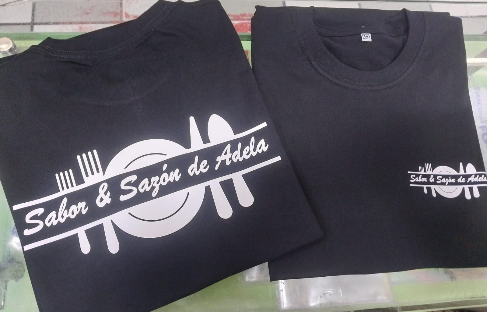 Dos camisetas negras con un gráfico blanco de un plato, un tenedor y una cuchara con el texto 
