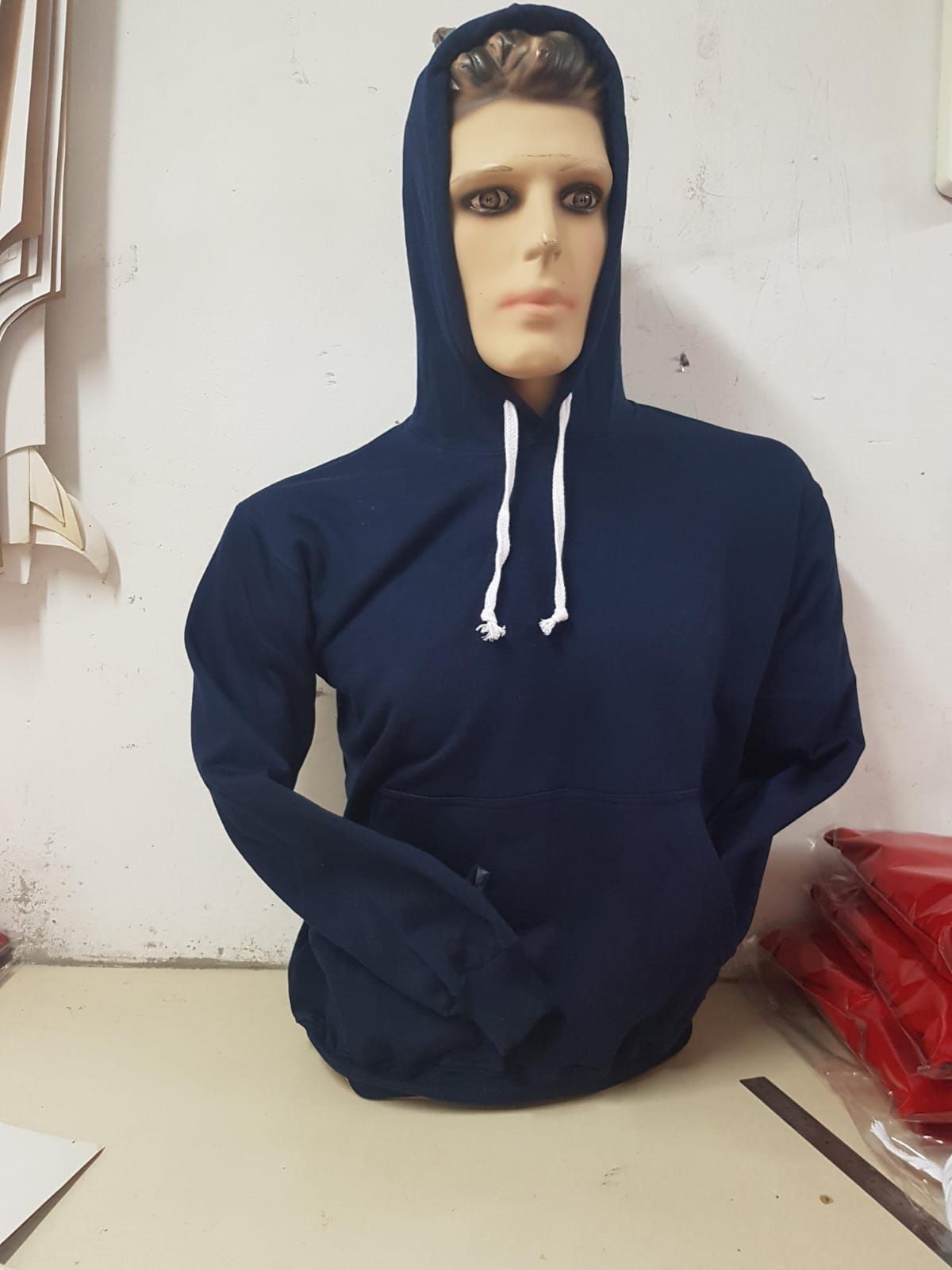 Un maniquí con una sudadera lisa azul marino con capucha y cordones blancos, colocado sobre una pared lisa.