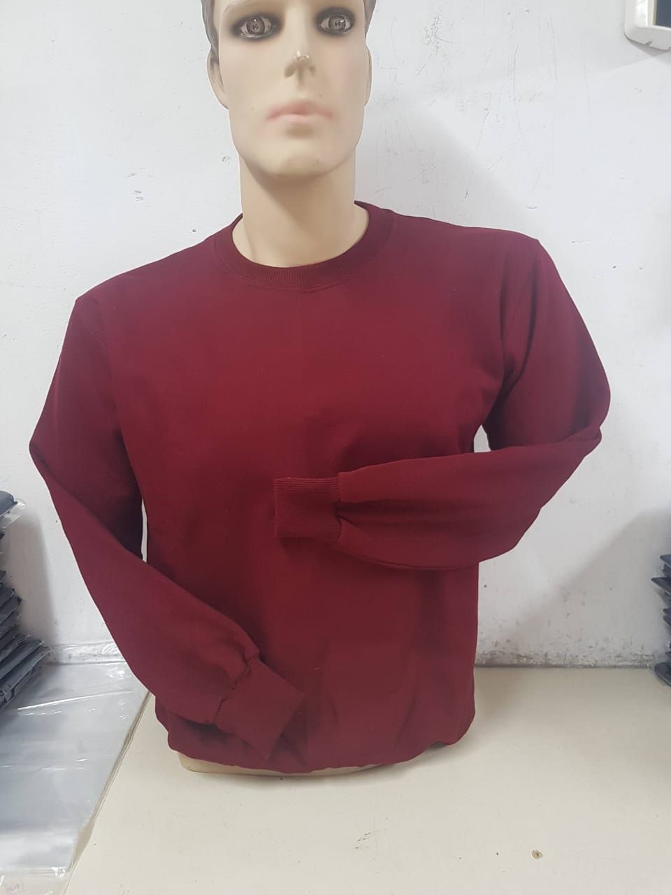 Un torso de maniquí con una sudadera de cuello redondo y manga larga de color burdeos liso sobre un fondo blanco liso.