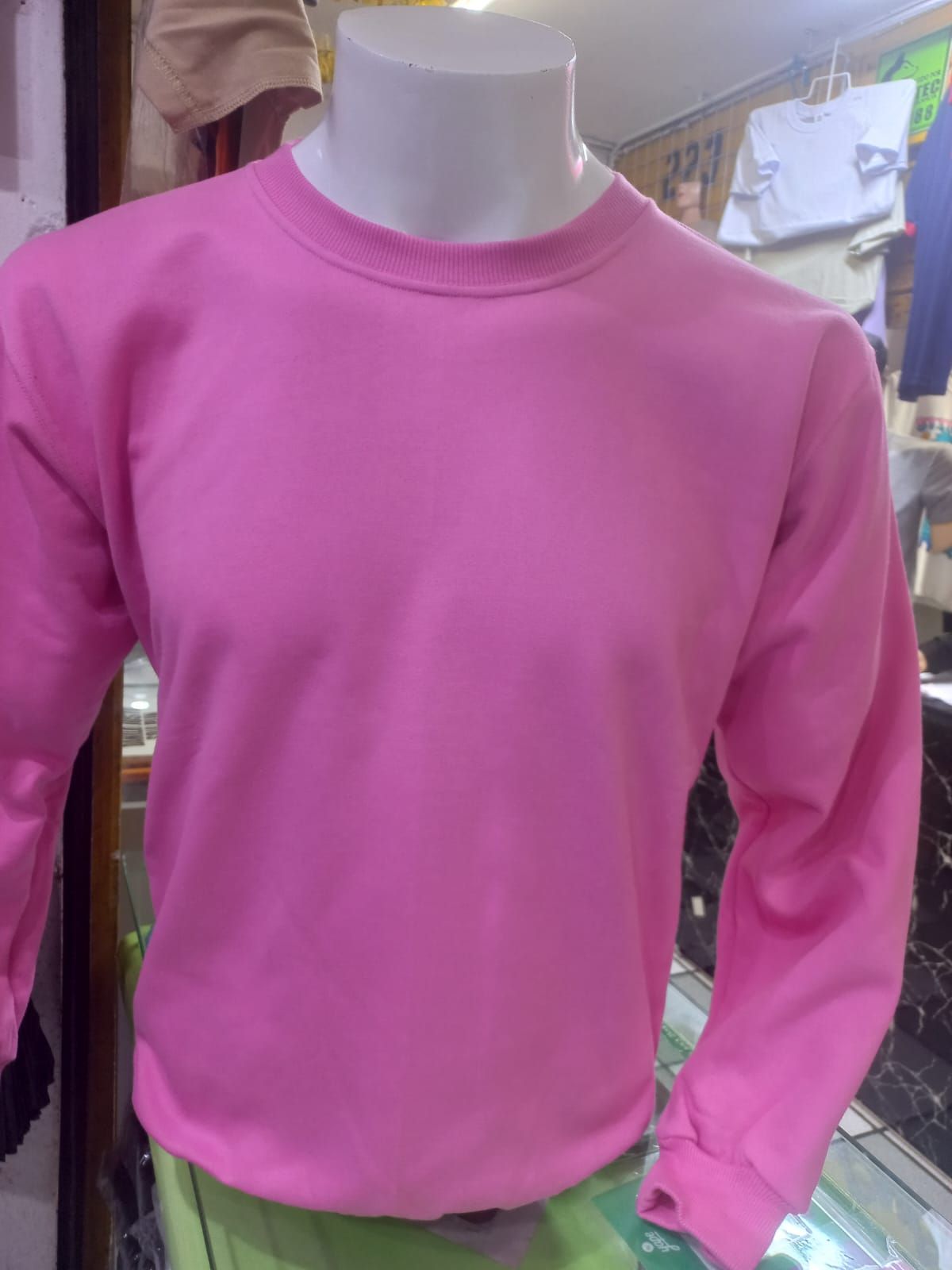 Una sudadera lisa de manga larga y cuello redondo, de color rosa brillante, expuesta en un maniquí en una tienda de ropa.