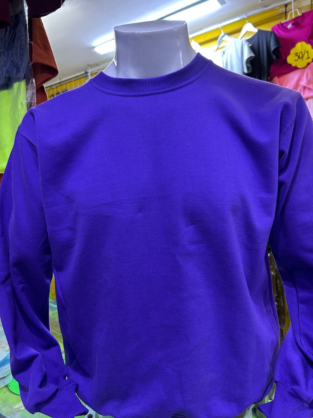 Una sudadera de manga larga y cuello redondo de color morado brillante, expuesta en un maniquí en una tienda de ropa.