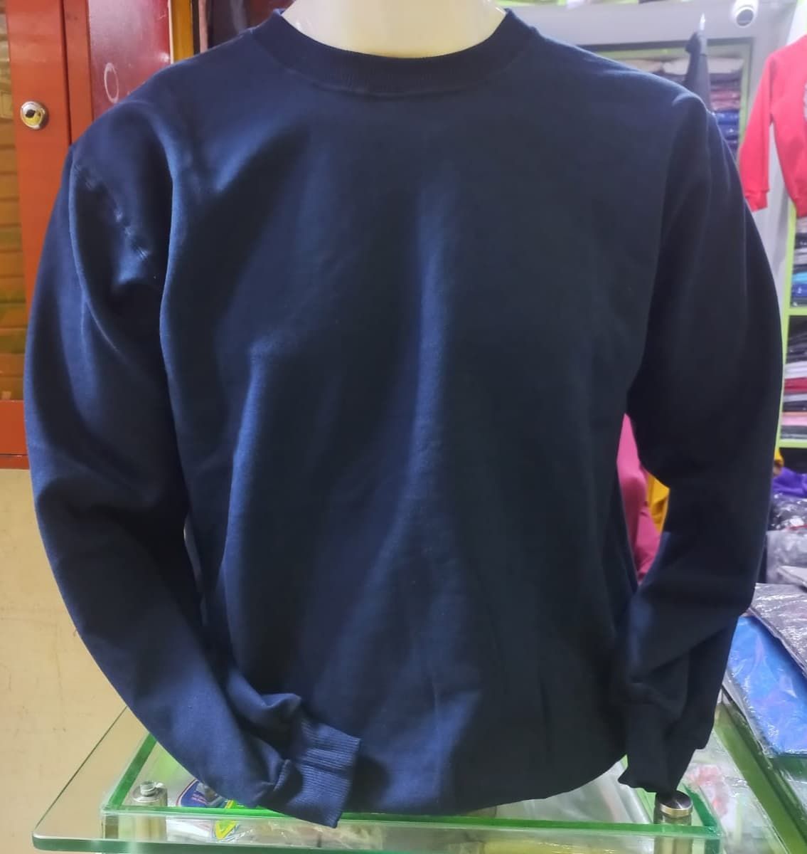 Una sudadera lisa de manga larga y cuello redondo de color azul marino, expuesta en un maniquí en una tienda.