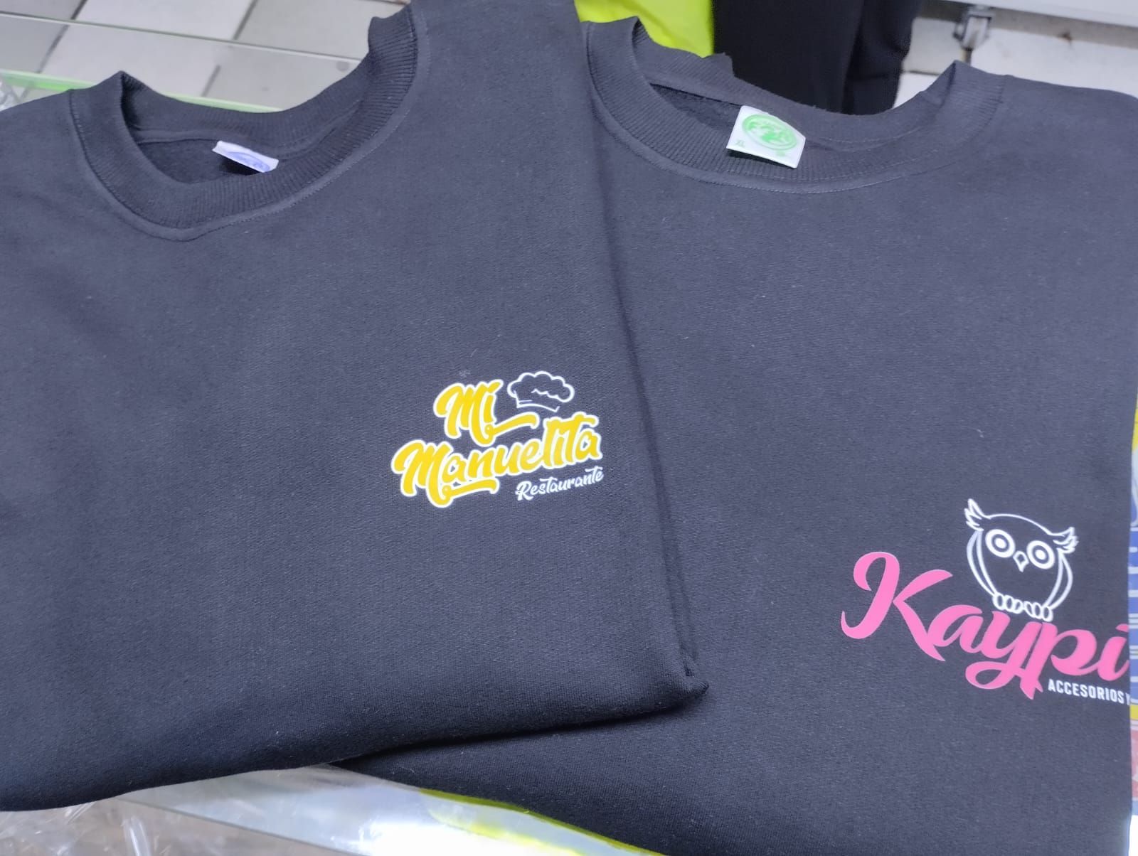 Dos camisetas negras dobladas con logotipos estampados