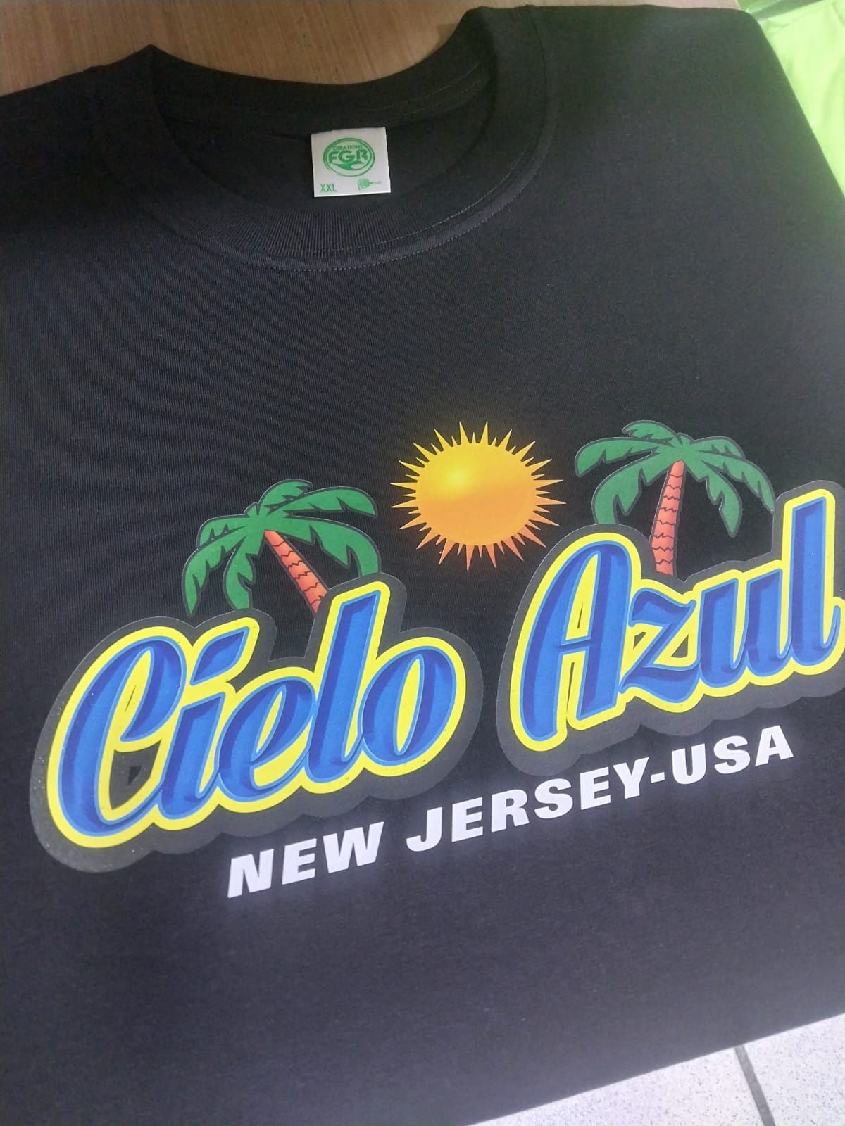 Camiseta negra con un gráfico de un sol amarillo entre dos palmeras sobre el texto 