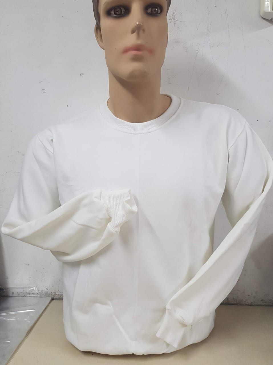 Una sudadera blanca lisa de manga larga y cuello redondo, exhibida sobre la cabeza y el torso de un maniquí de color neutro.