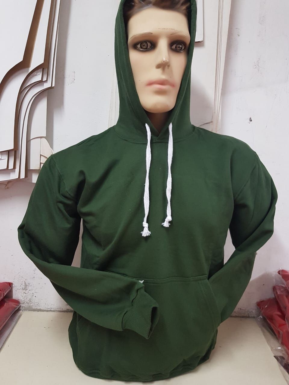 Una sudadera con capucha de color verde oscuro y cordones blancos en un maniquí.