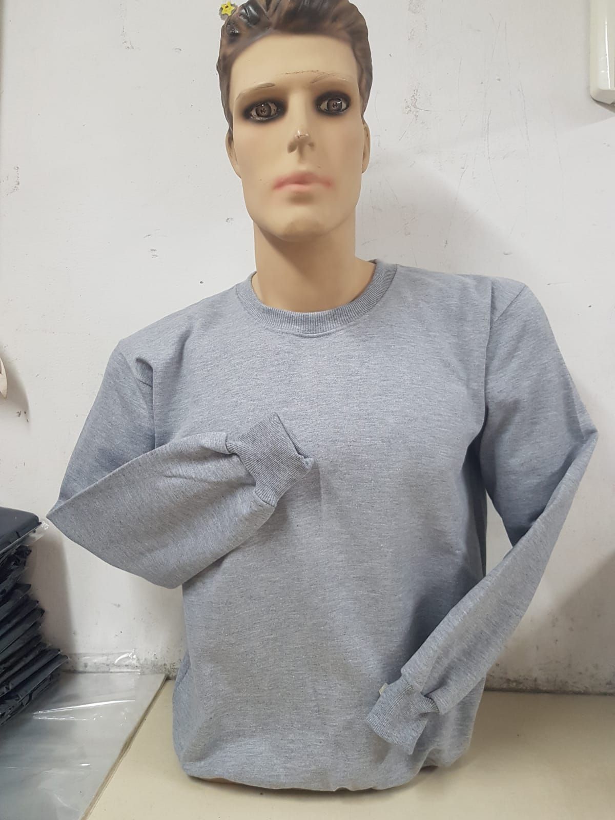 Una sudadera gris de manga larga y cuello redondo expuesta en un maniquí sin cabeza.
