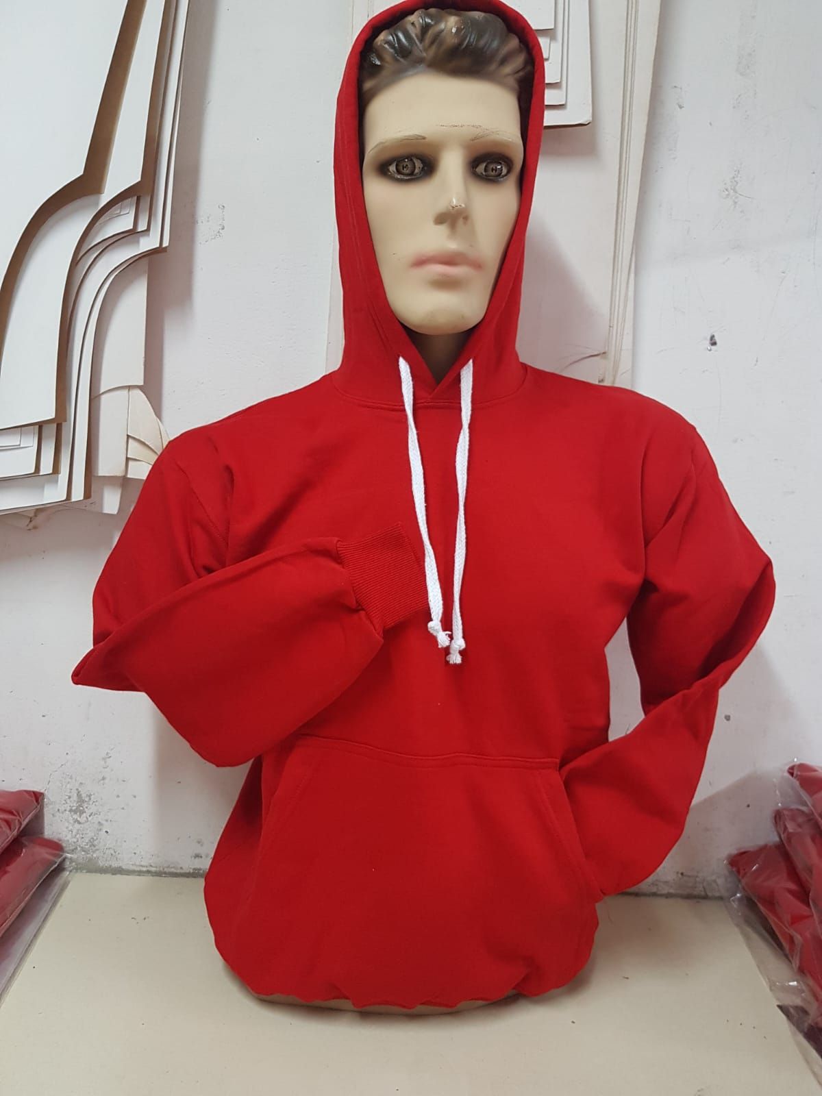 Una sudadera roja de manga larga con capucha y cordones blancos, expuesta en un maniquí.