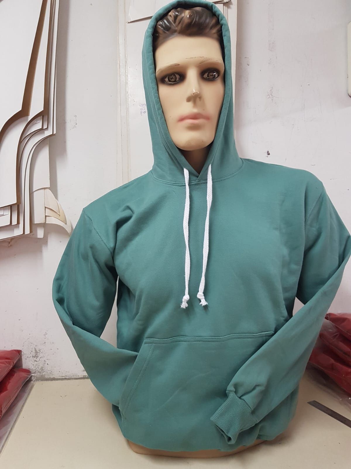 Un maniquí con una sudadera con capucha color turquesa y cordones blancos en un estudio o taller.