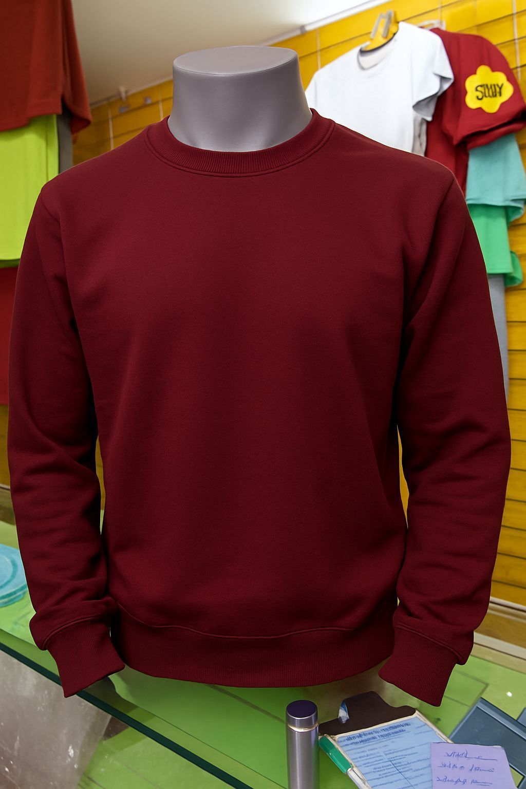 Una sudadera lisa de manga larga y cuello redondo de color granate, expuesta en un maniquí en una tienda.