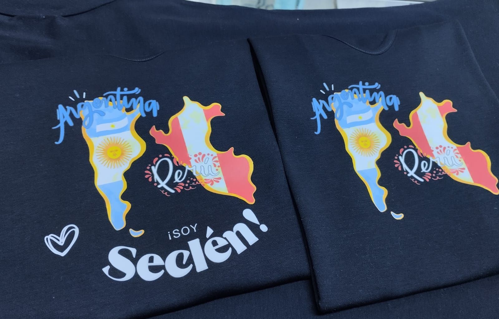 Dos camisetas negras con mapas de Argentina y Perú rellenos con sus respectivas banderas nacionales y el texto ¡Soy Seclén!
