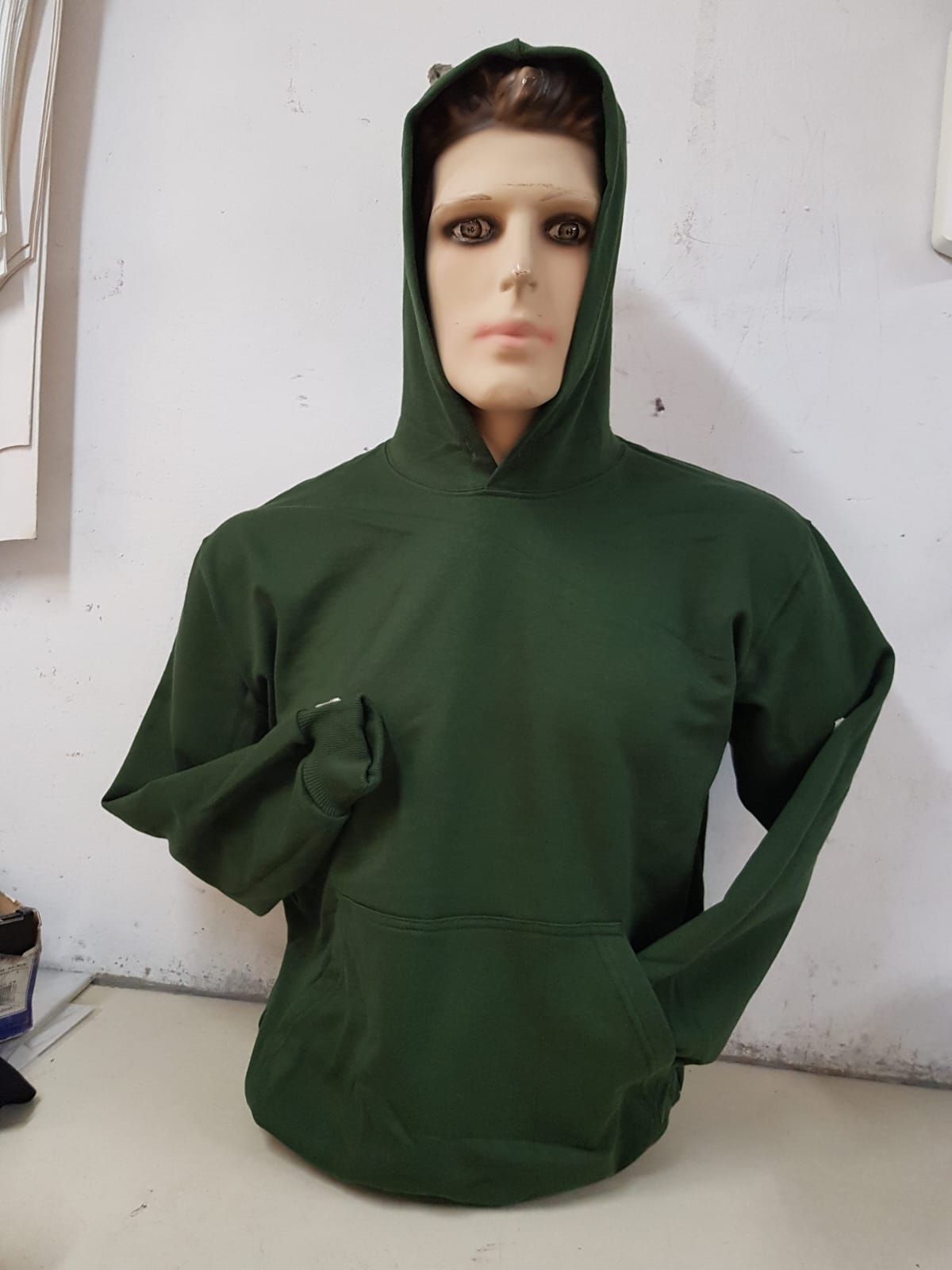 Una sudadera con capucha de manga larga de color verde bosque expuesta en un maniquí sobre una pared blanca lisa.