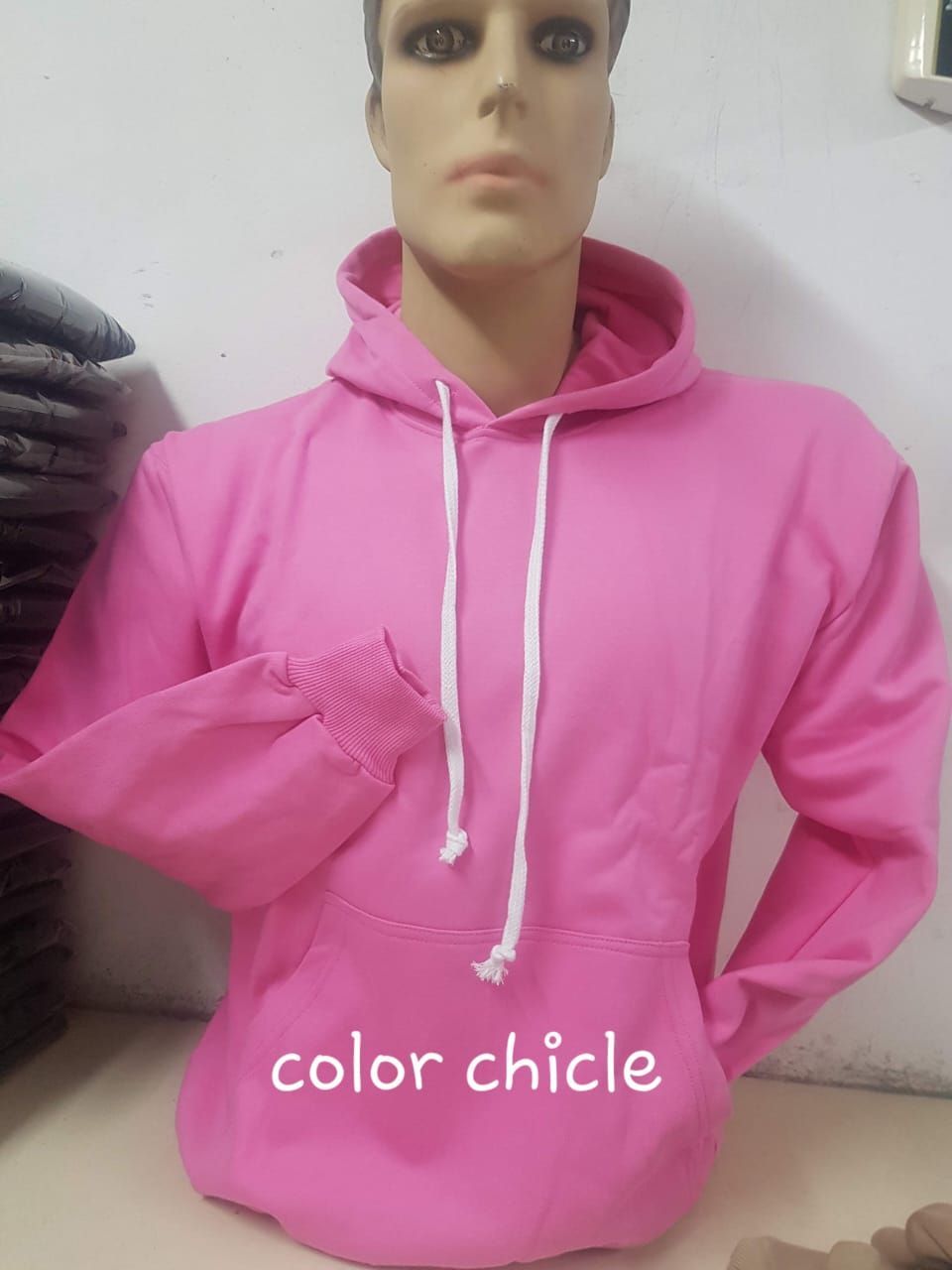 Una sudadera rosa con capucha sobre un maniquí, con mangas largas, bolsillo delantero y cordones blancos.