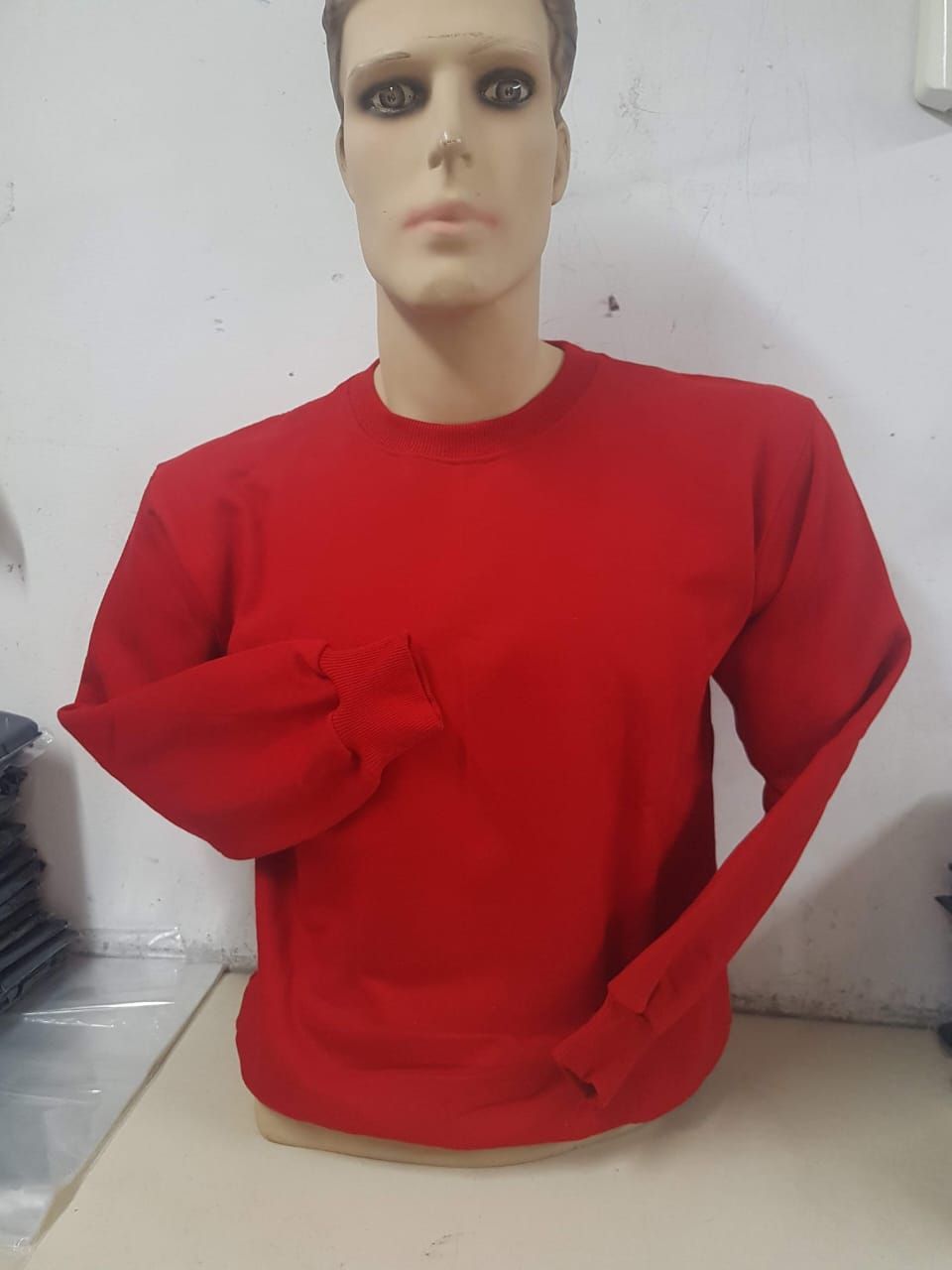 Un maniquí con una sudadera roja lisa de manga larga y cuello redondo sobre un fondo blanco liso.