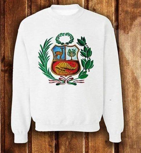 Una sudadera blanca con el colorido escudo de armas del Perú centrado en el pecho sobre un fondo de madera rústica.