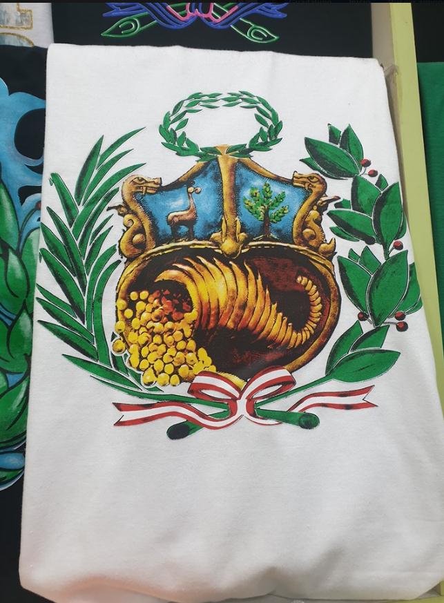 Una camiseta blanca con un estampado artístico y colorido del escudo de armas peruano con una cornucopia y ramas de laurel.