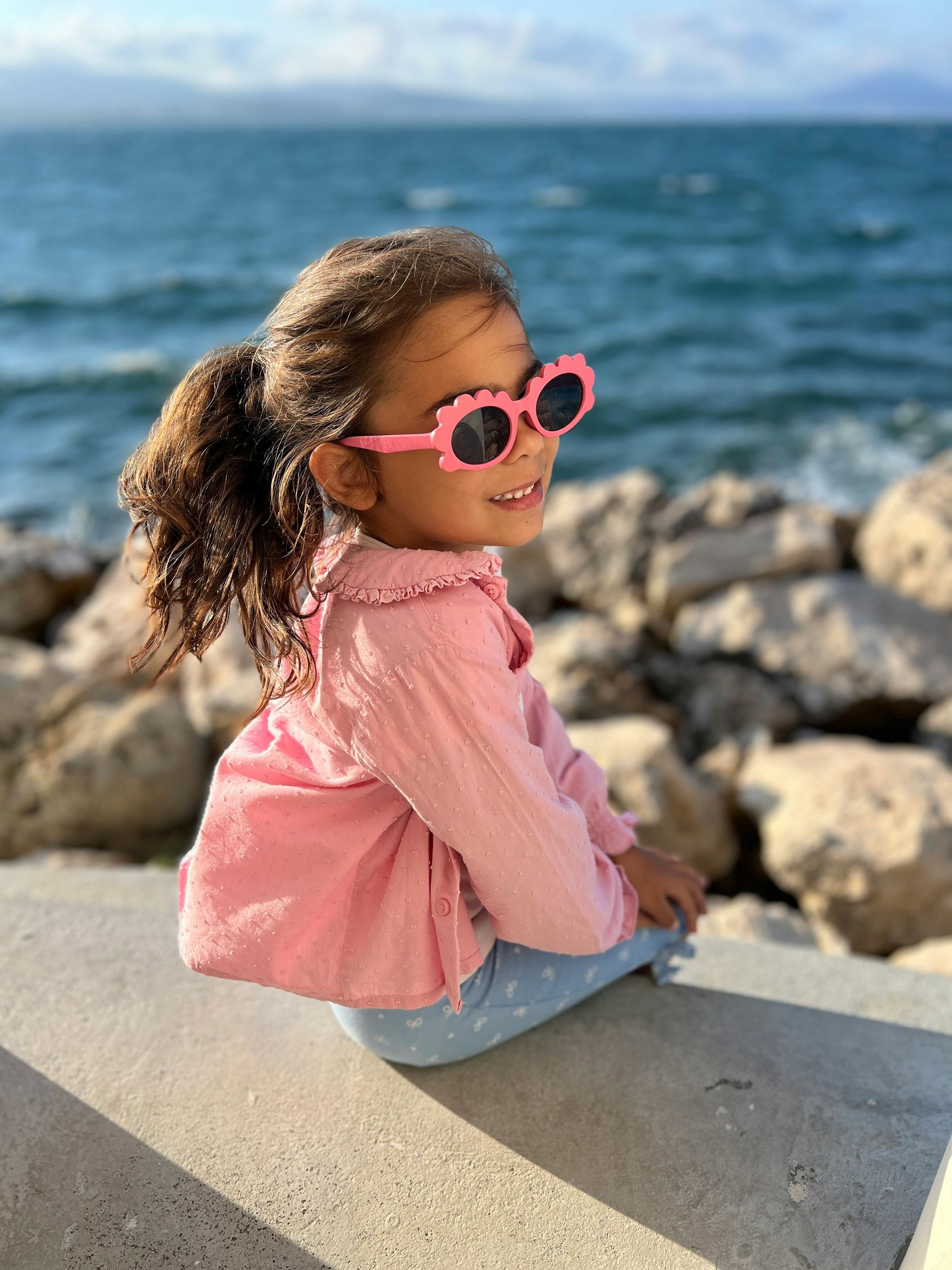 Una niña con cabello rizado lleva gafas de sol rosas 