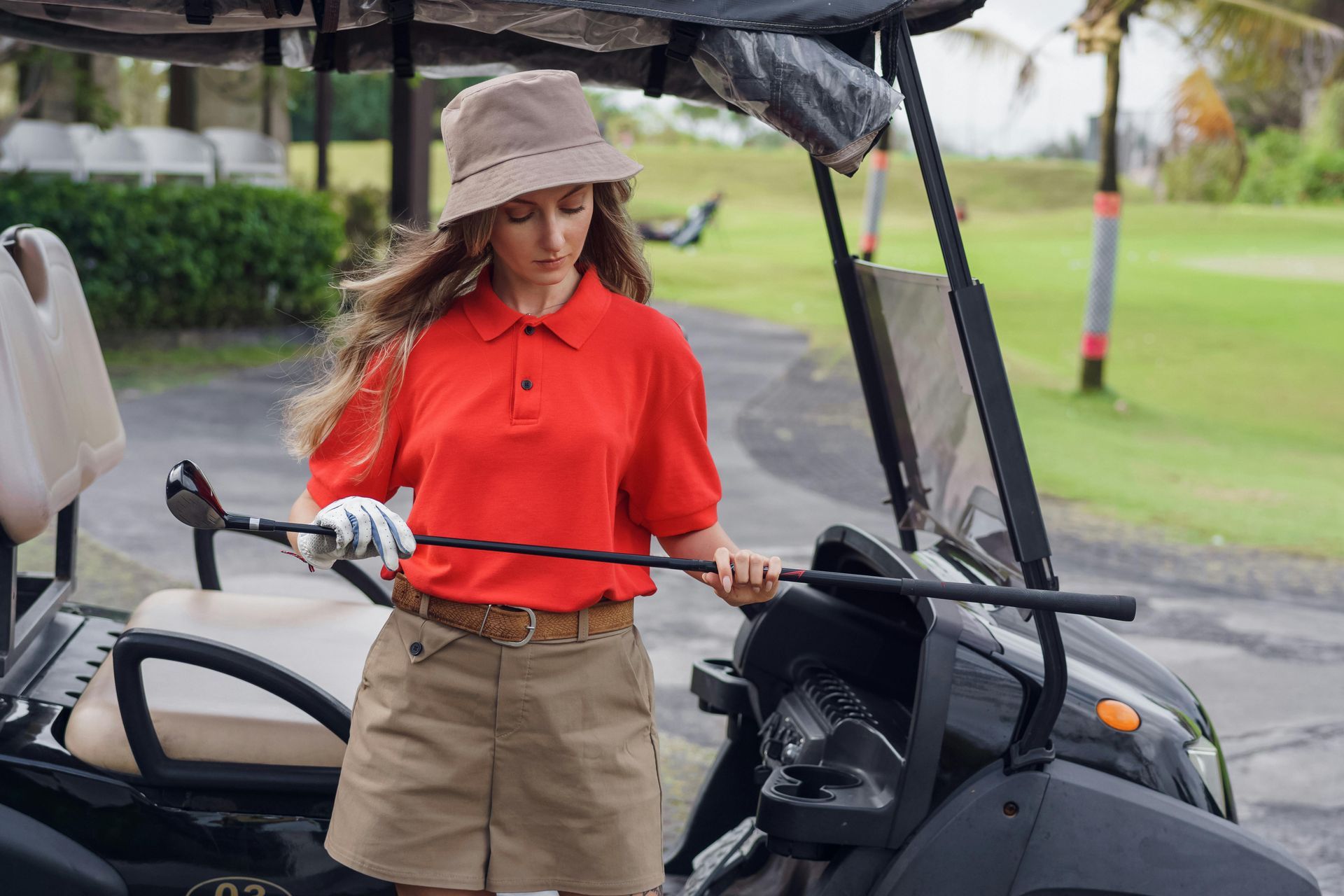 Un golfista con camisa roja y sombrero de pescador está de pie junto a un carrito 