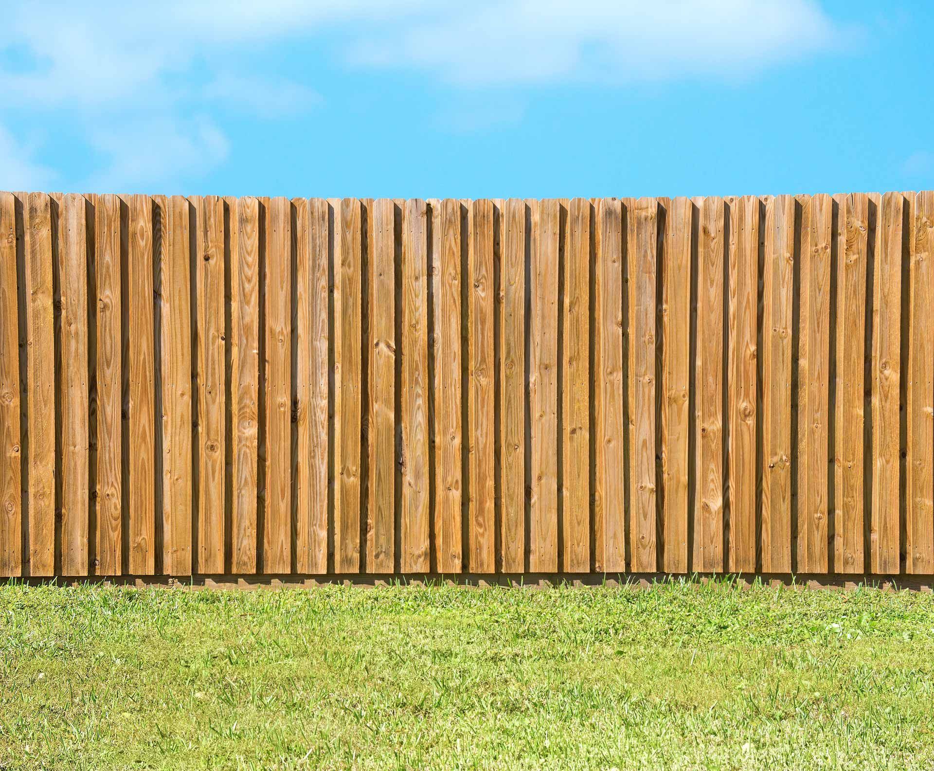 Wooden privacy fence installed by fence company on green lawn under blue sky. Wooden privacy fence installed by fence company on green lawn under blue sky.