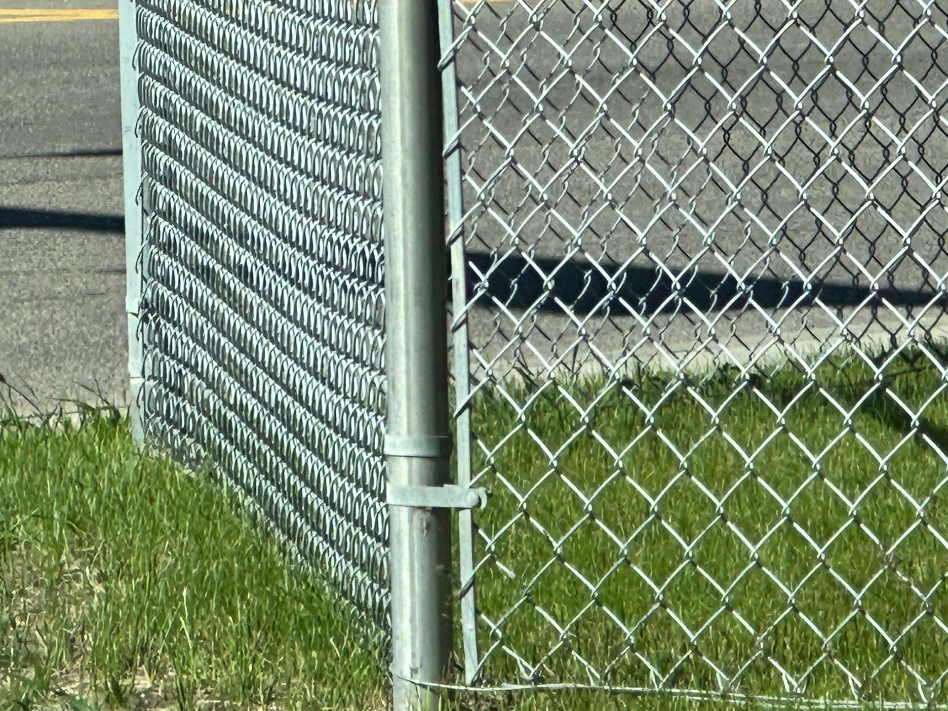 Commercial chain link fence with a galvanized metal post and gate hardware.