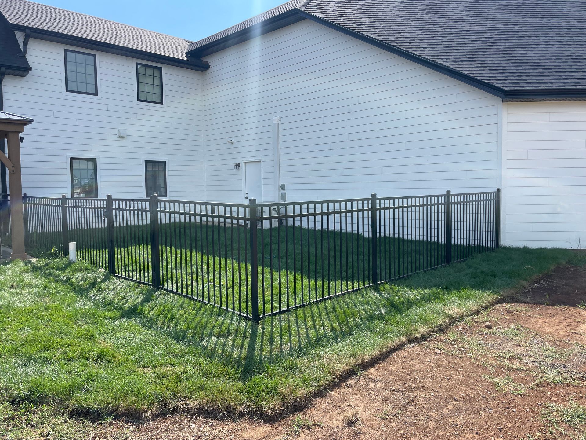 Black metal fence encloses a small grassy yard beside a white building.